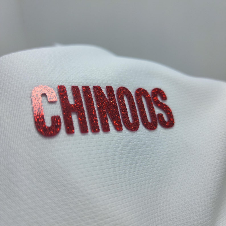May include: White fabric with the word "CHINOOS" in red glitter lettering.