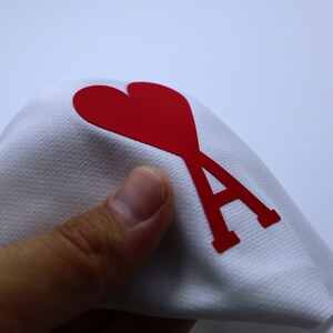 May include: White fabric with a red heart and the letter A printed on it.