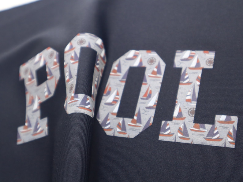 May include: A navy blue shirt with the word "POOL" printed in white letters. The letters are filled with a pattern of small sailboats.