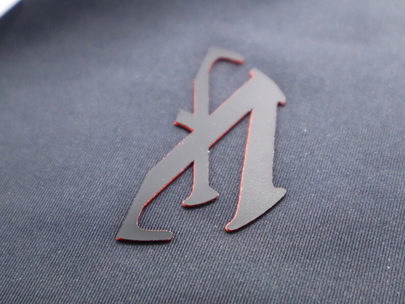 May include: A black letter "A" with a red outline, sewn onto a dark blue fabric.