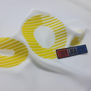 May include: White fabric with a yellow, striped, circular design. The fabric is folded and a black label with the text "YOUR LOGO HERE" is attached.
