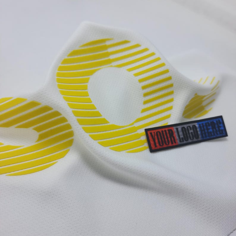May include: White fabric with a yellow, striped, circular design. The fabric is folded and a black label with the text "YOUR LOGO HERE" is attached.
