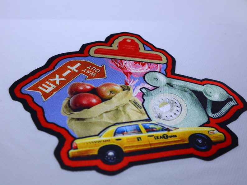 Peut inclure: Un patch rouge, noir et blanc avec un taxi jaune, une pomme rouge dans un sac en papier brun, un panneau bleu avec le texte "WAY OUT" et le texte cyrillique "Ш-1", et un t&eacute;l&eacute;phone &agrave; cadran vert.