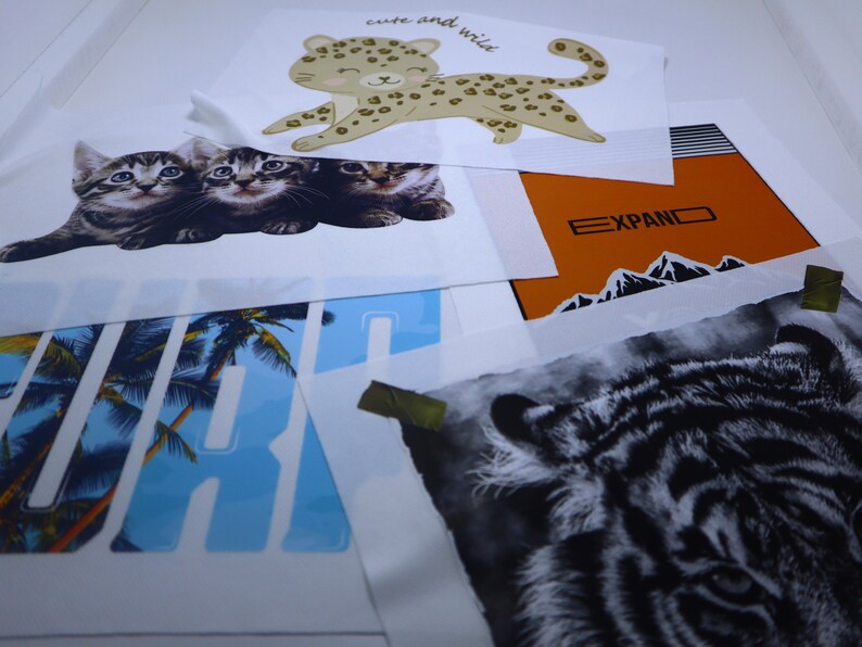 May include: A collection of iron-on transfers featuring various animal designs. The transfers include a leopard, a tiger, and three kittens. The transfers are on white paper and are ready to be applied to fabric.