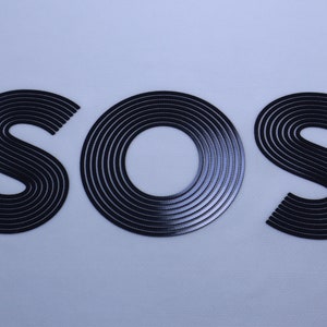 May include: A close-up of the word "SOS" written in black, with each letter made up of concentric circles.