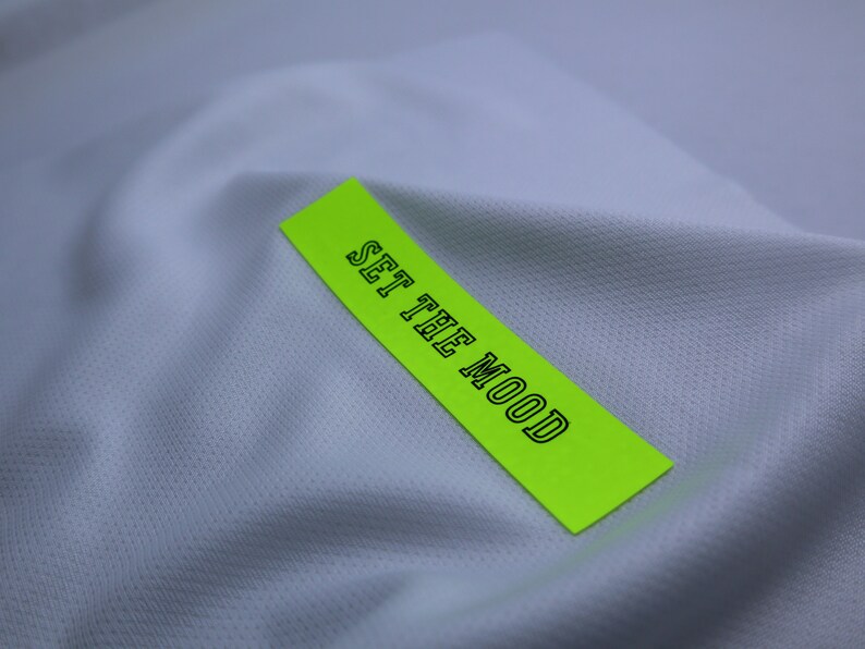 May include: A bright green label with the text "SET THE MOOD" in black outlined letters, placed on a white fabric background.
