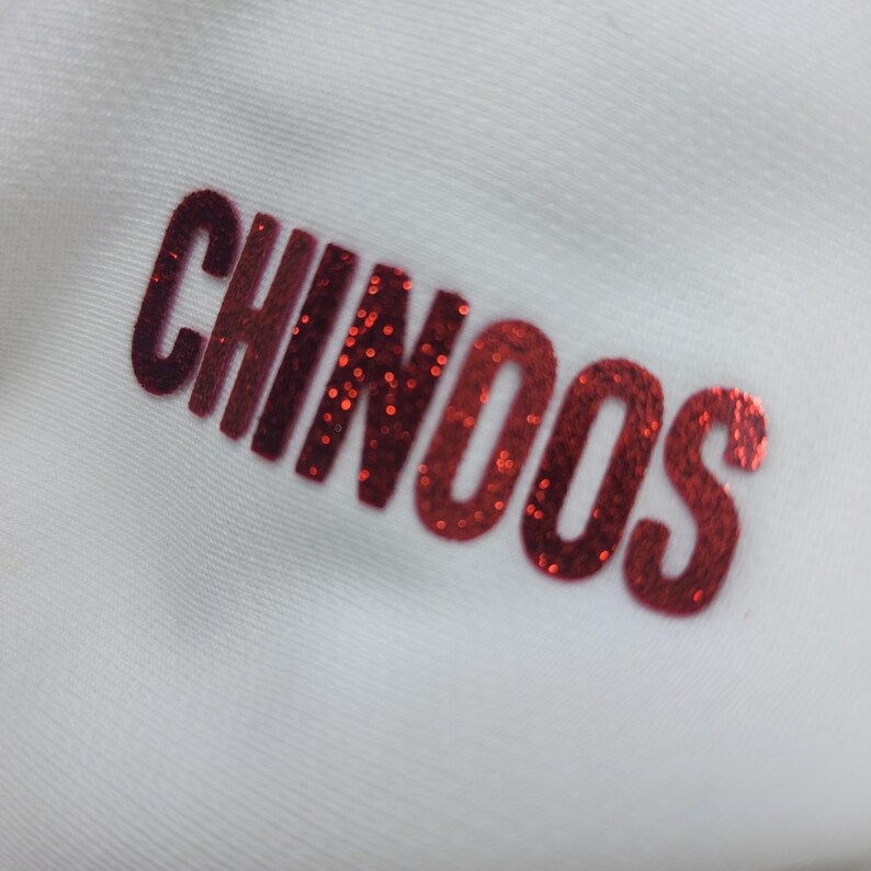 May include: Red glitter lettering on a white background that reads "CHINOOS".