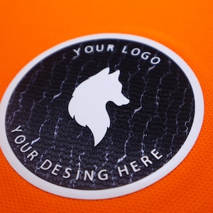 Op de afbeelding: Een witte ronde patch met een zwarte achtergrond en een wit wolfsilhouet. De tekst "YOUR LOGO" staat boven de wolf en "YOUR DESING HERE" staat onder de wolf.