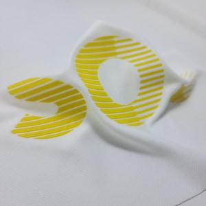 May include: White fabric with a yellow, striped, raised, rubberized letter "C" printed on it.