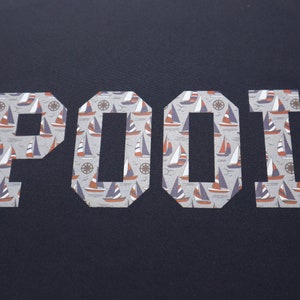 May include: A navy blue t-shirt with the word "POOL" printed in white letters. The letters are filled with a pattern of small sailboats.