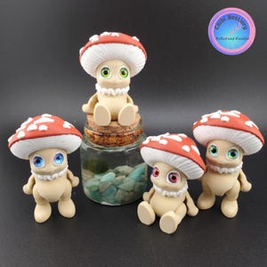 Puede incluir: Cuatro figuras caprichosas de hongos con sombreros rojos y blancos y ojos expresivos. Uno está sentado encima de un frasco de vidrio con tapa de corcho, mientras que los otros están de pie o sentados cerca. Las figuras tienen cuerpos color canela.