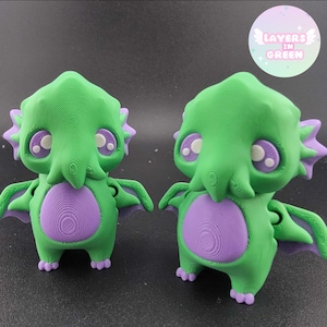 May include: Two green and purple figurines of a cartoon monster with large eyes, tentacles, and wings. The figurines have a circular purple belly and are standing upright. The text "LAYERS IN GREEN" is in a circle in the background.