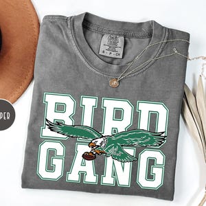 May include: A gray t-shirt with a white graphic of a green eagle with the text "BIRD GANG" in white.