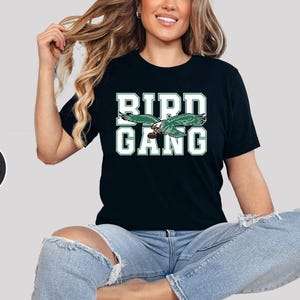 May include: A black t-shirt with a green and white graphic of a bird with the text "BIRD GANG" on it.