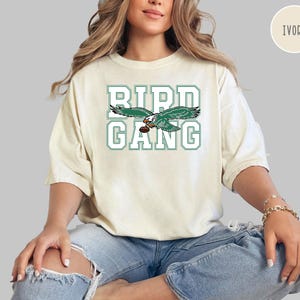 May include: Ivory t-shirt with a green and white graphic of a bird with the text "Bird Gang".