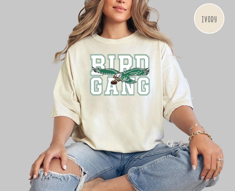 May include: Ivory t-shirt with a green and white graphic of a bird with the text "Bird Gang".