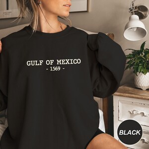 Op de afbeelding: Zwart sweatshirt met de witte tekst "GULF OF MEXICO - 1569 -". De crew neck sweatshirt is effen zwart van kleur. De tekst is gecentreerd op de borst.