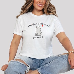 Pode incluir: Camiseta branca com um gr&aacute;fico de um gato e o texto "who's afraid of little old me? you should be"