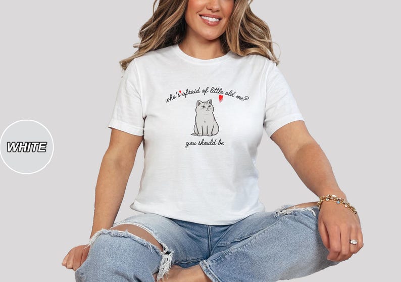 Pode incluir: Camiseta branca com um gr&aacute;fico de um gato e o texto "who's afraid of little old me? you should be"