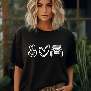 May include: Black t-shirt with a white peace sign, heart, and a Jeep with an American flag on the front.