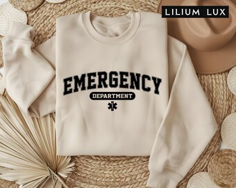 May include: A beige sweatshirt with the text "EMERGENCY DEPARTMENT" in black with a black star of life symbol.