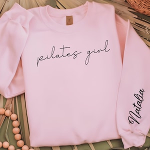 May include: A pink sweatshirt with the text "pilates girl" on the front and the name "Natalia" on the sleeve.