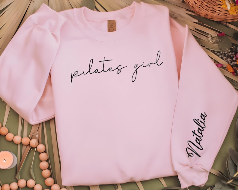 May include: A pink sweatshirt with the text "pilates girl" on the front and the name "Natalia" on the sleeve.