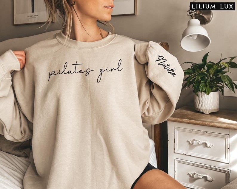 May include: A beige sweatshirt with the text "pilates girl" on the front and the name "Natalia" on the sleeve.