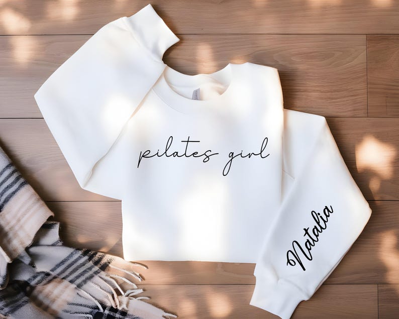 May include: White sweatshirt with the text "pilates girl" in black script on the front and the name "Natalia" in black script on the sleeve.