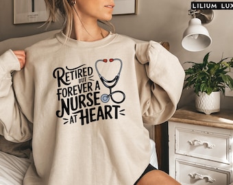 May include: A beige sweatshirt with the text "Retired but forever a nurse at heart" and a stethoscope graphic.