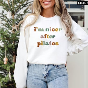 May include: White sweatshirt with the text "i'm nicer after pilates" in colorful letters.