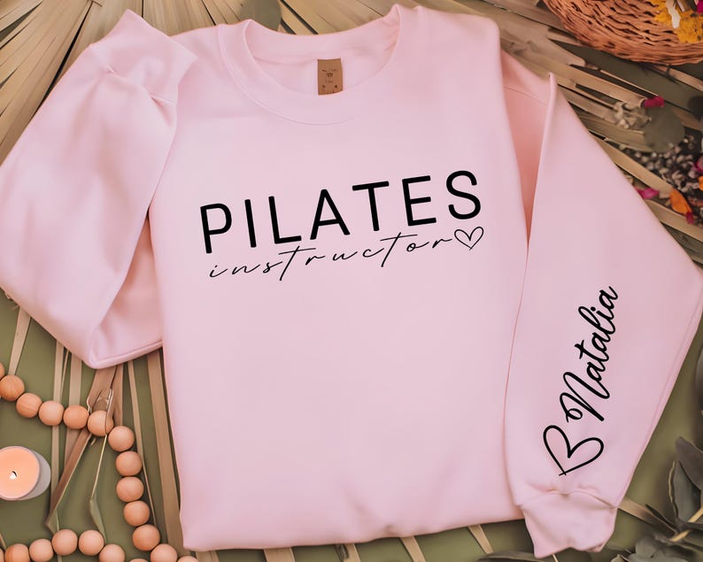 May include: Pink sweatshirt with the text "PILATES instructor" and a small heart on the front. The left sleeve has the name "Natalia" written on it.