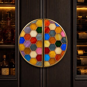 May include: A pair of decorative cabinet door handles. Each handle is a half-circle with a gold-coloured frame and a mosaic of colourful, hexagonal glass pieces. The handles are mounted on a dark wood cabinet.