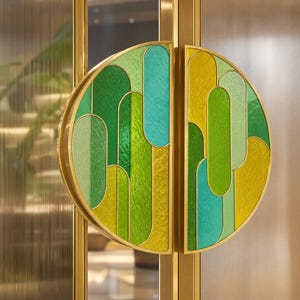 May include: Decorative door handles with a stained glass design. The handles are semi-circular, with a gold frame and a mosaic of green, yellow, and teal glass. The door frame is gold, and the glass door has a vertical striped pattern.