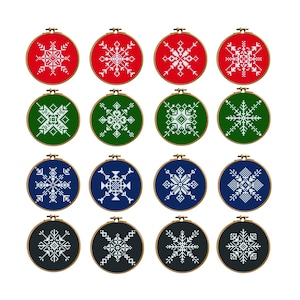May include: Twelve embroidered snowflake designs in wooden hoops. The snowflakes are white, set against red, green, blue, and black backgrounds. The embroidery hoops are arranged in a grid pattern.