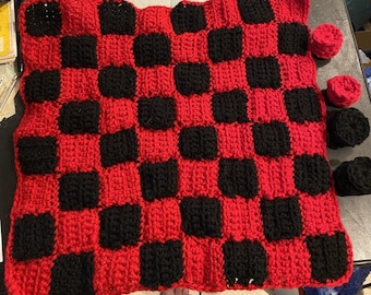 May include: A red and black crocheted checkerboard game with black crocheted game pieces.
