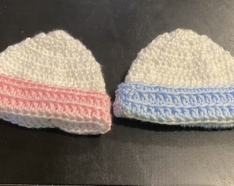 Könnte beinhalten: Zwei gehäkelte Mützen, eine mit einem rosa Band und eine mit einem blauen Band.