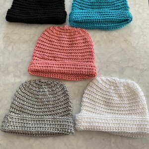 Puede incluir: Cinco gorros de ganchillo en diferentes colores: negro, turquesa, rosa, gris y blanco. Los gorros están hechos con el mismo patrón de punto y tienen un diseño simple y clásico.