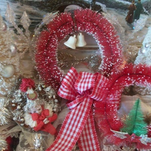 May include: A red and white gingham ribbon bow with two red and white flocked wreaths, two white flocked Christmas trees, and a small white flocked Christmas tree with a red and white dressed doll.