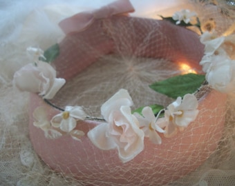 May include: A pink hat with a white net and a floral trim. The flowers are made of white fabric and are arranged in a circle around the hat.