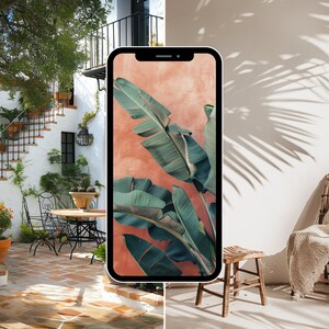 May include: A smartphone displaying a tropical leaf wallpaper with a peach background. The phone is in front of a white wall with a wooden chair and a white throw blanket.