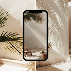 May include: A smartphone displaying a photo of a minimalist interior with a wooden chair and a small table. The photo is taken from a low angle, showing the shadows of palm leaves on the wall.