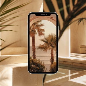 May include: A smartphone displaying a photo of palm trees and a beach with a blue sky and white clouds. The phone is on a white surface with a palm leaf in the foreground.
