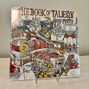 May include: The Book of Taliesyn vinyl record album cover by Deep Purple features a detailed, colorful illustration of a medieval castle, a chessboard with pieces, a bird, a rabbit, and a fish, with text listing band members.