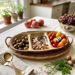 May include: An oval, three-section ceramic serving dish with a rooster illustration in the center compartment. The dish features a cream-colored glaze with brown trim and two woven wicker handles, resting on a matching oval wicker tray.