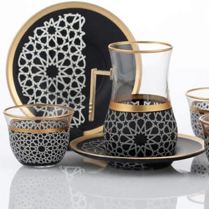 Può includere: Servizio da tè nero e oro con motivo geometrico a stella bianca. Il set include tazze, piattini e una tazza con manico. I bordi e le maniglie sono dorati. Ideale per servire tè o caffè.