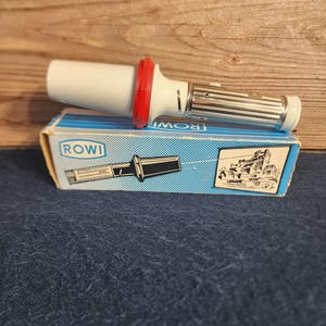 May include: A white and silver flashlight with a red and white plastic ring around the lens. The flashlight is in its original box, which is blue and white with the word "ROWI" printed on it.