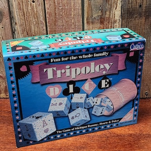 May include: A Tripoley game box with a blue background and the words "Tripoley" and "Fun for the whole family." The box includes dice and a pink dice cup. The game is "The Game of Michigan Rummy, Hearts & Poker."