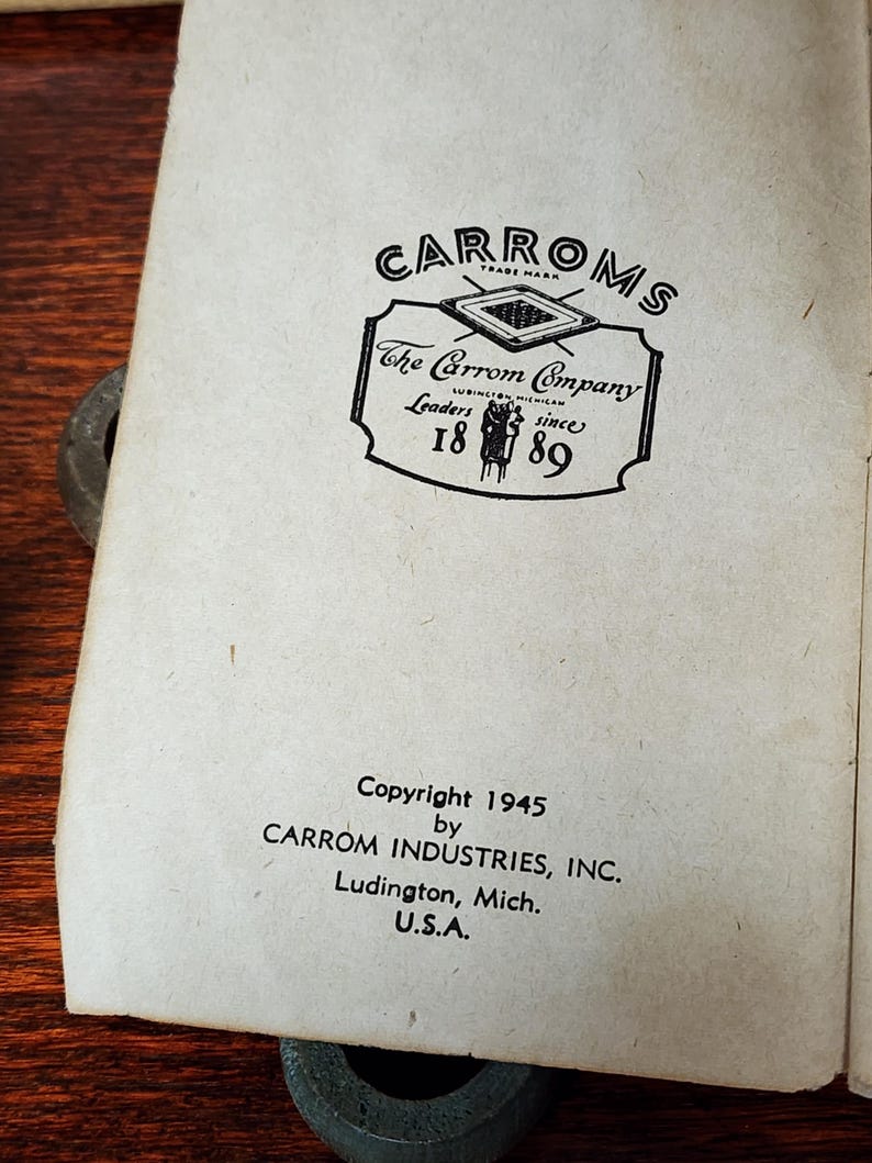 May include: Black and white image of a vintage Carrom Company logo with the text "CARROMS", "The Carrom Company", "Leaders since 1889", and "Copyright 1945 by CARROM INDUSTRIES, INC. Ludington, Mich. U.S.A."