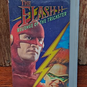 May include: A vintage VHS tape for "The Flash II: Revenge of the Trickster." The cover features a comic book style illustration of the Flash in a red suit and mask, and the Trickster in a green mask. The background is blue with a yellow lightning bolt.